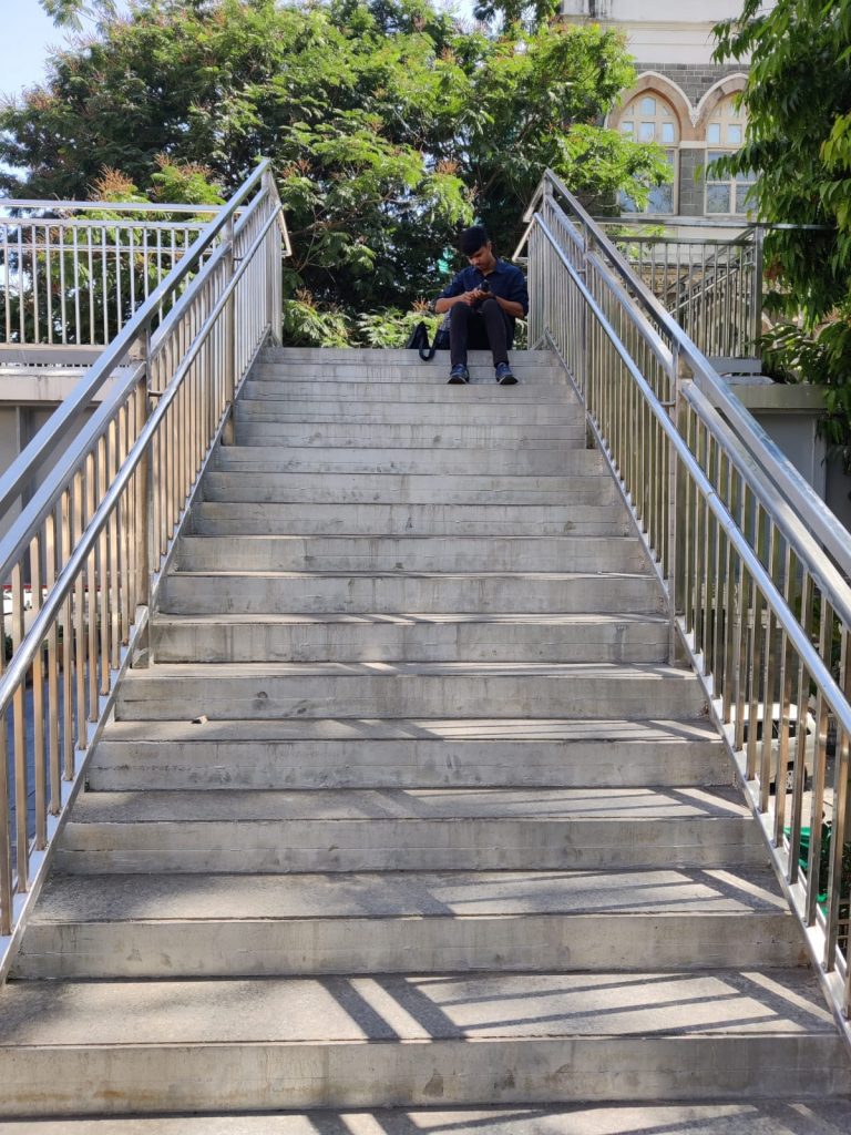 A passer-by relaxes on the staircase of the bridge amidst Mumbai’s sultry heat